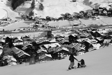 Two snowboarders on snowy ski slope in high winter mountains and sunlit village