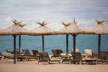 Straw beach umbrellas and wooden sun beds on a sandy beach against the sea. Beach infrastructure in Bulgaria with the inscription: 