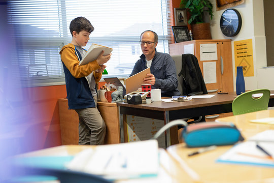 Junior High Student And Teacher Talking At Desk In Classroom