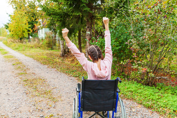 Young happy handicap woman in wheelchair on road in hospital park enjoying freedom. Paralyzed girl...