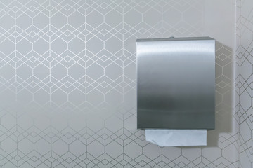 silver metal paper towel bathroom dispenser on an elegant white gray wallpaper patter that is...