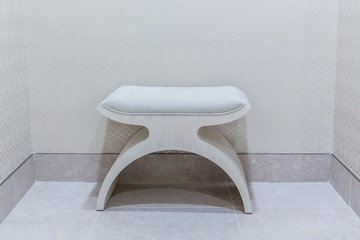 Single modern stool seat along a plain neutral wall in a clean and bare environment