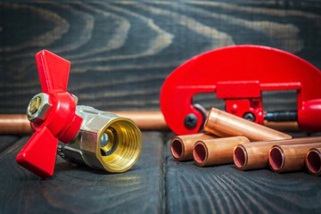 Water ball valve with red handle and copper pipes for plumbing repairs on black vintage wooden...
