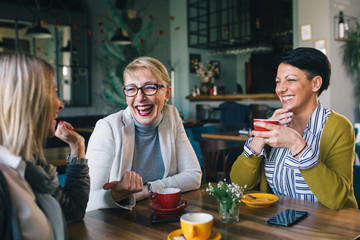 mid aged woman friends enjoying time drinking coffee in cafe