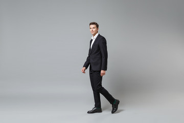 Fototapeta na wymiar Side view of confident young business man in classic black suit shirt posing isolated on grey wall background in studio. Achievement career wealth business concept. Mock up copy space. Looking camera.