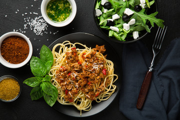 Dining table concept. Spaghetti Bolognese and arugula salad, olives and feta cheese.