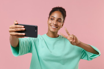 Smiling young african american woman girl in green sweatshirt isolated on pastel pink background....