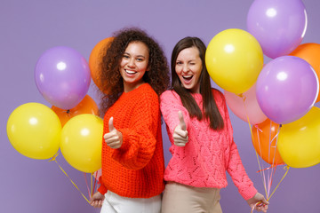 Cheerful two european african american women friends in knitted sweaters isolated on violet purple...