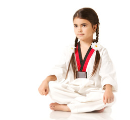 Girl in white kimono with accessories in form of daisies on pigtails, sitting in yoga pose on white background and looking away