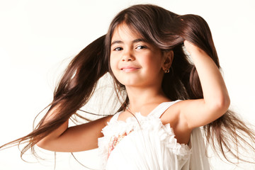 Smiling girl buried hands in her long brown hair, dressed in white blouse, isolated on white background and looking at camera