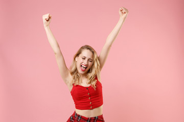 Naklejka premium Happy young blonde woman girl in red sexy clothes posing isolated on pastel pink wall background. People lifestyle concept. Mock up copy space. Rising hands, doing winner gesture, keeping eyes closed.