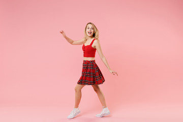 Side view of excited young blonde woman girl in red sexy clothes posing isolated on pastel pink wall background in studio. People lifestyle concept. Mock up copy space. Looking camera spreading hands.