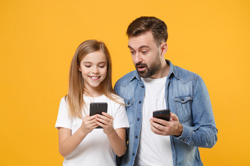 Amazed bearded man in casual clothes with child baby girl. Father little kid daughter isolated on yellow background. Love family day parenthood childhood concept. Use mobile phone typing sms message.