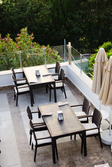 Wattled tables and chairs on terrace summer cafe overlooking the green park.