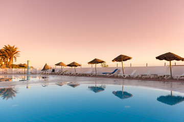 Swimming pool with sunbeds and umbrellas reflected in the water at sunset, Tunisia