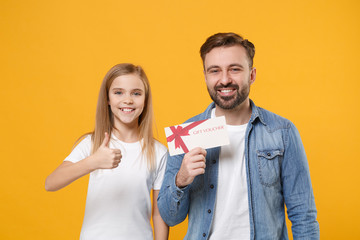 Bearded man in casual clothes with child baby girl. Father little kid daughter isolated on yellow wall background. Love family day parenthood childhood concept. Hold gift certificate showing thumb up.