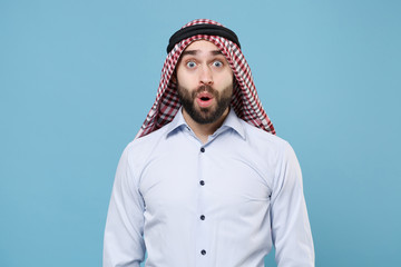 Amazed bearded young arabian muslim man in keffiyeh kafiya ring igal agal casual clothes isolated on pastel blue background. People religious lifestyle concept. Mock up copy space. Keeping mouth open.