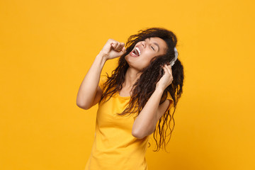 Funny young african american woman in casual t-shirt posing isolated on yellow background. People lifestyle concept. Mock up copy space. Listen music with headphones, sing song, keeping eyes closed.