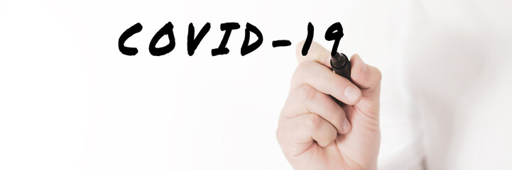 Hand of a businessman writing a word covid-19 with black marker in a conceptual image of corona virus outbreak.