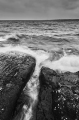 Black and white photo waves rushing in over stones and rocks