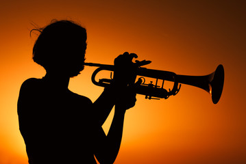 Silhouette of a Young woman plays trumpet on sunset.