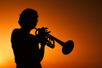 Silhouette of a Young woman plays trumpet on sunset.