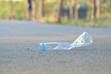 A plastic bottle of drinking water littering on the street ground floor at the green park with blurred a group of trash containers on the sidewy and green nature background 