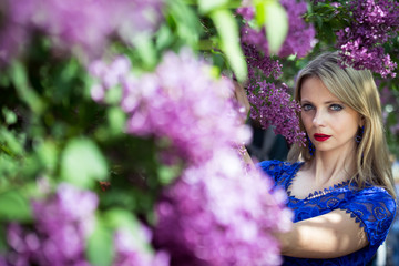 Naklejka premium Blond girl in blooming lilac, horizontal orientation, looking at the camera.