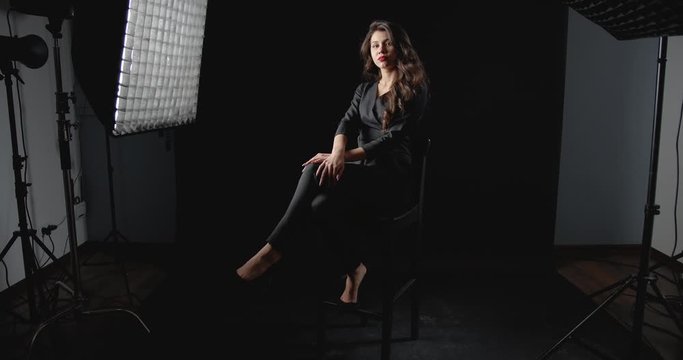 Confident beautiful woman in black fashionable suit posing to camera in dark photo studio