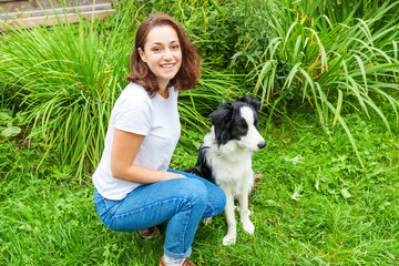 Naklejka na ściany i meble Smiling young attractive woman playing with cute puppy dog border collie in summer garden or city park outdoor background. Girl training trick with dog friend. Pet care and animals concept.