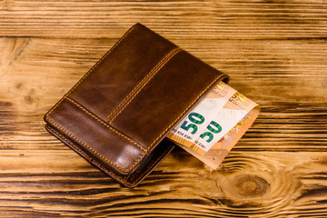 Brown leather wallet with fifty euro banknotes on the wooden background