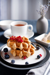 Belgian waffles with blueberries and red currants, honey and tea on a white table.