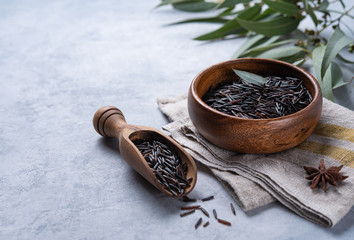 black  rice in wood  bowl on line napkin with spoon  on a light gray background