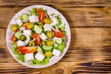 Ceramic plate with greek salad on wooden table. Top view
