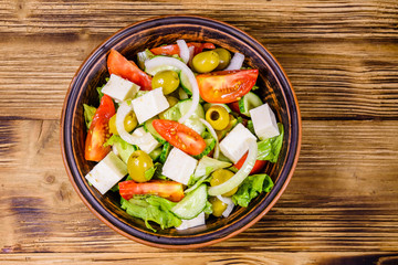 Ceramic plate with greek salad on wooden table. Top view