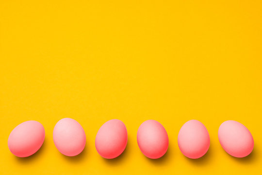 a row of pink colored eggs on yellow background with copyspace on top