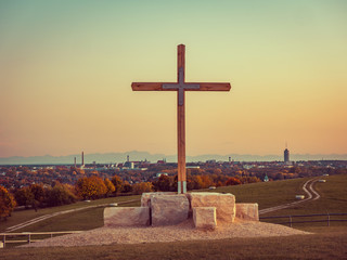 Panorama image of Augsburg skyline during sunset with mountains in the background and wooden cross in the front