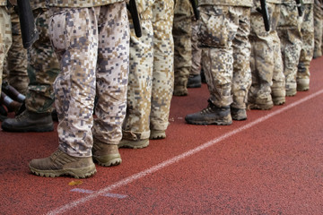 Section of soldiers legs in military uniform and boots standing in line at camp
