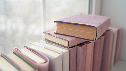 Large stack of books on windowsill. Books wrapped in colored paper lie on window sill.