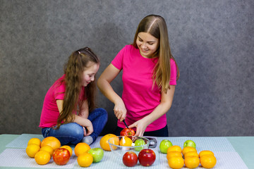 Fototapeta na wymiar daughter and mom cut a fruit salad consisting of apple orange and mandarin