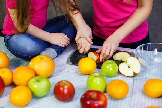 Daughter And Mom Cut A Fruit Salad Consisting Of Apple Orange And Mandarin