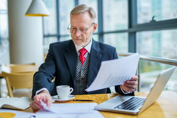 Businessman checks a printed report or document when he sits, working on paper work at a laptop.