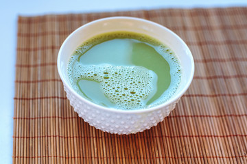 Green matcha tea in a white bowl on bamboo mat. Soft focus, Top view