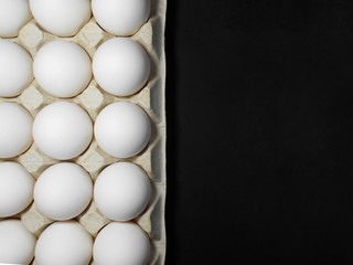 Raw chicken eggs in egg box on black background.