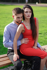 Fototapeta na wymiar Beautiful couple of man and woman sitting on a bench in a park. Romantic theme with a girl and a guy. Spring Summer theme relationship, love, Valentine's day