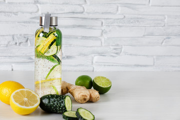 Detox infused water with lemon, lime, ginger and cucumber in a glass sport bottle on white wooden...