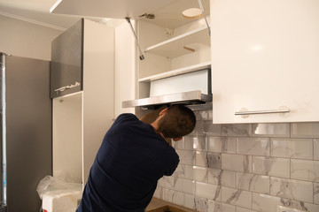 back view of young handyman fixing extractor range hood kitchen