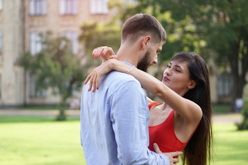 Fototapeta premium Beautiful couple of man and woman against the backdrop of a beautiful park and city architecture. Romantic theme with a girl and a guy. Spring Summer picture relationship, love, Valentine's day