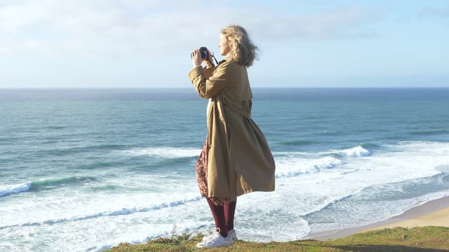 tall woman approaches ocean and takes photos of nature