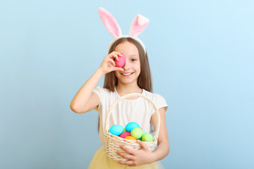 Portrait of a little cute smiling girl with bunny ears and an Easter basket in hands on a colored background. Easter background with place to insert text.